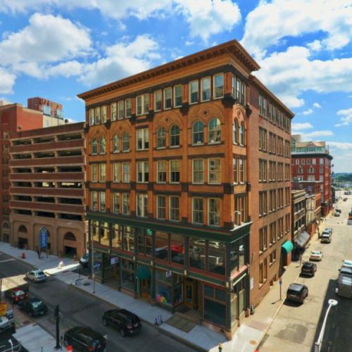 A street view of an urban area features a brown building at the intersection, cars parked along the street, and a partially visible multilevel parking structure.