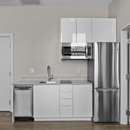 This image shows a modern kitchen with white cabinets, a stainless steel refrigerator, microwave, dishwasher, and a small sink.