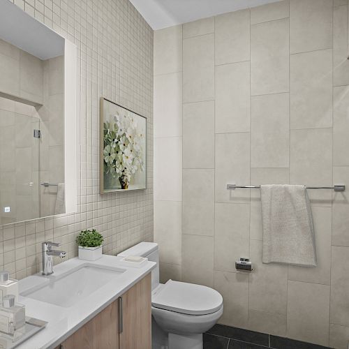 This image shows a modern bathroom with beige tiles, a mirror above the sink, a toilet, a towel on a rack, and a glass shower enclosure.